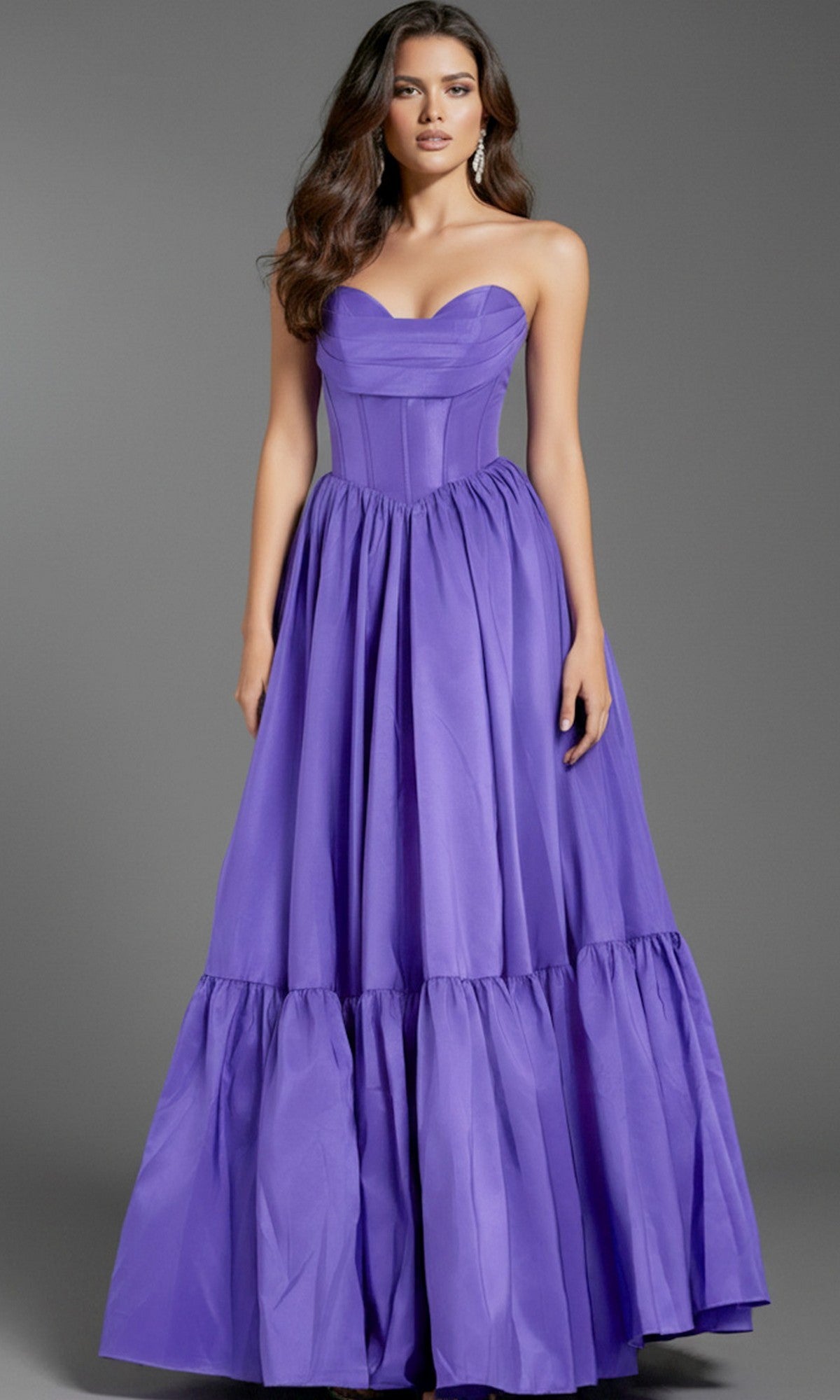 A woman wears the Jovani 47883 Strapless Long Ruffled Prom Dress in purple, featuring a sweetheart neckline, corset-style bodice, and a full tiered skirt, standing before a plain gray background.